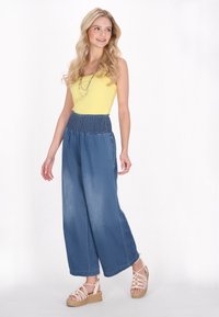 Sárga ujjatlan felső, széles szárú kék farmernadrággal, smockolt derékkal és bézs espadrille platform szandállal párosítva.
