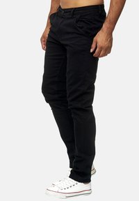 Czarne bawełniane spodnie o dopasowanym kroju, z kieszeniami z przodu i subtelnymi detalami stębnowania, w połączeniu z białymi sneakersami.