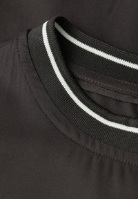 Collo di un indumento nero realizzato in tessuto strutturato con una doppia striscia bianca. Il collo è arrotondato, presenta cuciture ordinate e una caduta morbida.