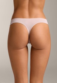 Kvinde iført lyserøde seamless g-strengs trusser set bagfra mod en neutral baggrund.