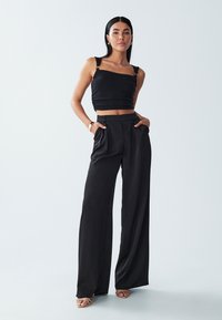 Sort cropped top med justerbare stropper, parret med højtaljede, brede sorte bukser. Glat stof med en subtil glans.