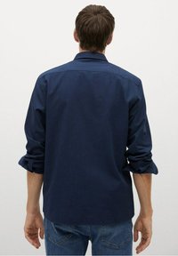Granatowa koszula na guziki z podwiniętymi rękawami, dopasowany krój i gładka faktura. Widok od tyłu, pokazujący kołnierz i szwy na ramionach.