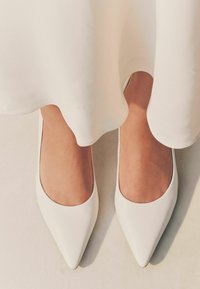 Ballerines blanches à bout pointu en cuir lisse. Les chaussures présentent un design de cou-de-pied bas et une esthétique épurée et minimaliste.