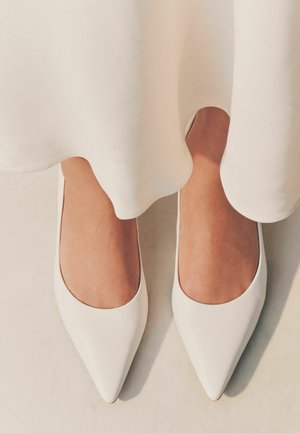 Valkoiset kärjelliset ballerinat, jotka on valmistettu sileästä nahasta. Kengissä on matala vampsuunnittelu ja puhdas, minimalistinen esteettisyys.