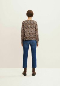 Top a maniche lunghe con stampa floreale su sfondo nero, jeans blu con leggero svaso all'orlo e stivali alla caviglia marroni.