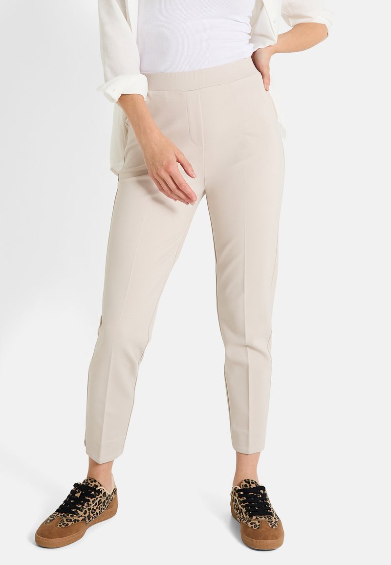 Pantalons beiges au design ajusté avec des détails de couture à l'avant, associés à des baskets à imprimé animal avec des lacets noirs et des accents en daim.