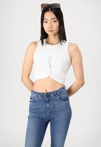 Vit, kort ärmad topp med en knutdetalj fram, ihopparad med högmidjade blå denimjeans med fickor och knäppning.