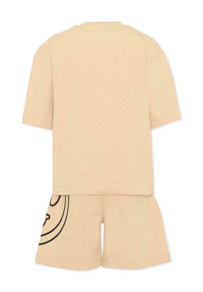 Camiseta beige de manga corta combinada con pantalones cortos a juego que presentan un gráfico circular negro parcial en la pierna izquierda.