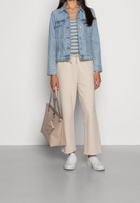 Ljusblå denimjacka, randig topp i grönt och vitt, beige vida byxor, vita sneakers, bär en beige handväska med kedjehandtag.