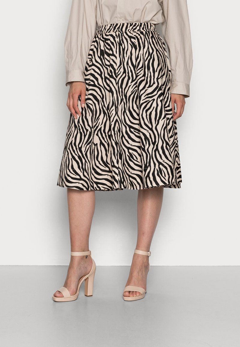 Beige rok tot op de knie met zwarte zebrastripes, voorzien van een elastische tailleband. Gecombineerd met beige, gestripte hoge hakken.