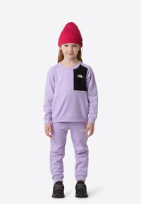 Lila Fleece-Sweatshirt mit schwarzem Einsatz, rundem Ausschnitt und gerippten Bündchen. Kombiniert mit passenden Jogginghosen und einer roten Strickmütze.