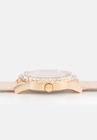Roségoldene Uhr mit einem runden Gehäuse, verziertem Ziffernblatt und einem glatten rosa Lederarmband. Verfügt über eine einfache Krone für Anpassungen.