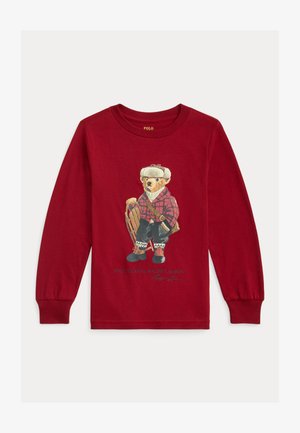 Rdeča majica z dolgimi rokavi z motivom medveda v karirasti srajci, ki drži sani, z rdečimi in črnimi poudarki ter belim napisom spodaj.