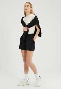 Pantalones cortos negros con cinturilla elástica, combinados con una blusa crema. Se lleva un suéter azul marino holgadamente sobre los hombros. Zapatillas blancas y calcetines de caña corta.