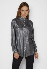 Metallisch graues Hemd mit Kunst-Krokodillederstruktur, durchgehender Knopfleiste, zwei Brusttaschen und langen Ärmeln. Glatte Oberfläche mit schimmerndem Aussehen.