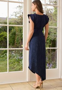 Abito blu navy, fino al ginocchio, con maniche a sbuffo corte e motivo testurizzato a foglie. Orlo asimmetrico e chiusura con cerniera nascosta sul retro.