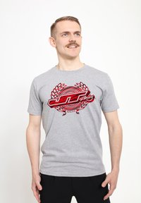 Šedé bavlněné tričko s červeným grafickým designem, na kterém je závodní logo a vavřínové listy. Krátké rukávy; klasický kulatý výstřih.