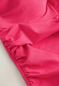 Élénk rózsaszín anyag, sima textúrával és az egyik szélén gyűrt részletekkel, puha és rugalmas kialakítással.