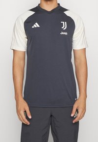 Camiseta atlética gris oscuro con mangas cortas blancas, diseño en forma de v, logo de Adidas en el hombro izquierdo y logo de Juventus en el pecho.