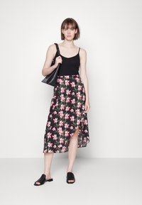 Saia preta floral com padrão de flores rosa e verdes, apresentando uma fenda lateral. Combinada com um top preto sem mangas e sandálias pretas planas.