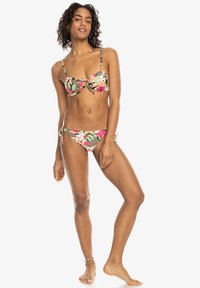 Ensemble de bikini avec un motif floral en rose, vert et beige. Le haut présente un détail en nœud ; le bas se noue sur les côtés pour un ajustement réglable.