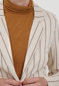 Krémový pruhovaný blazer s hnědými pruhy, zkombinovaný s hořčicovým rolákem. Blazer má vypasovaný střih a upravené klopy.