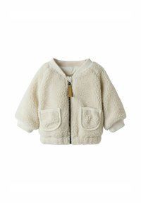 Veste en polaire de couleur crème, dotée d'une fermeture éclair à l'avant, de poignets côtelés et de deux poches avant, avec une texture douce et une coupe décontractée.