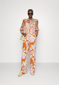 Blusa floreale con maniche arricciate in arancione, crema e rosa; pantaloni a gamba larga abbinati con motivi paisley e floreali; abbinati a una borsa crema.