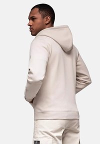 Lys beige hoodie lavet af glat stof, med h�ætte og ribbede manchetter. Båret med lyse bukser, der viser en afslappet pasform.