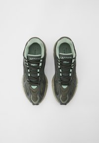 Lacoste sneakers feature a dark green mesh and leather upper, mint green accents, round toe, and textured rubber sole with detailed stitching.