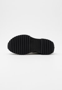 Semelle en caoutchouc noir d'une chaussure avec des rainures horizontales profondes et "CONVERSE" embossé au centre pour la traction et la prise.