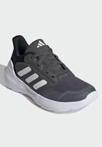 Schwarze Sportschuhe aus grauem Netzstoff, mit drei weißen Streifen an der Seite, gepolsterter Kante und einer weißen Gummisohle. Verfügt über strukturierte Materialien.