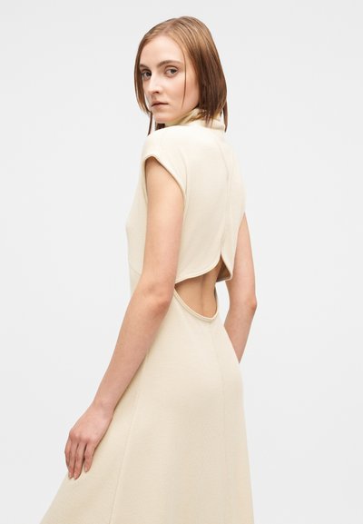 Μπεζ αμάνικο φόρεμα με ψηλή λαιμόκοψη, άνοιγμα στην πλάτη και ρέουσα γραμμή. Κατασκευασμένο από μαλακό, υφασμένο ύφασμα.