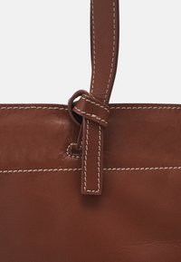 Brown leather handbag close-up featuring accent stitching, a loop detail on the strap, and a smooth texture.