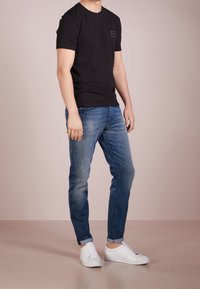 Camiseta de algodón negra de manga corta, combinada con unos vaqueros de mezclilla azul claro y zapatillas blancas. Diseño sencillo con un pequeño logo en la camiseta.