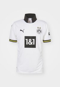 Bela športna majica z black ovratnikom in kratkimi rokavi, ki vsebuje rumene poudarke, Puma logotip in velik črn okvir z logotipom "1&1".
