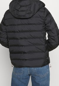 Black puffer jacket with a hood, features quilted design and elastic cuffs. The back shows a cinched hem and minimalistic style.