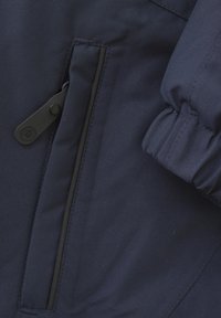 Marinblå jacka med en slät textur, som har en dragkedjeficka på sidan och elastiska ärmslut för en tät passform.