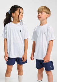 Vita kortärmade sporttröjor med svart chevronlogotyp på bröstet, i kombination med marinblå shorts och knähöga vita strumpor.