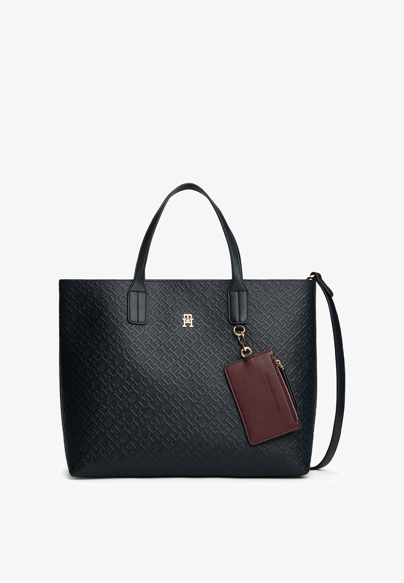 Zwarte, met textuur afgewerkte tote bag met dubbele handgrepen, gouden logo en een afneembare bordeauxrode kaarthouder die is bevestigd met een gouden ketting.
