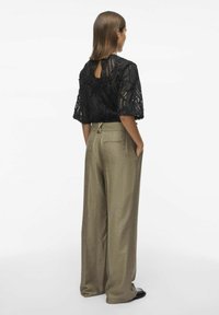 Top de encaje negro con mangas cortas y un detalle de abertura en la espalda, combinado con pantalones de pierna ancha de color marrón claro. Tejido texturizado con un diseño intrincado.