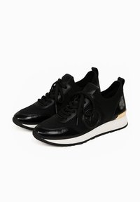 Zwarte sportschoenen met een mix van gestructureerd mesh en glad leer, met een witte tussenzool en een gouden accent op de hiel.