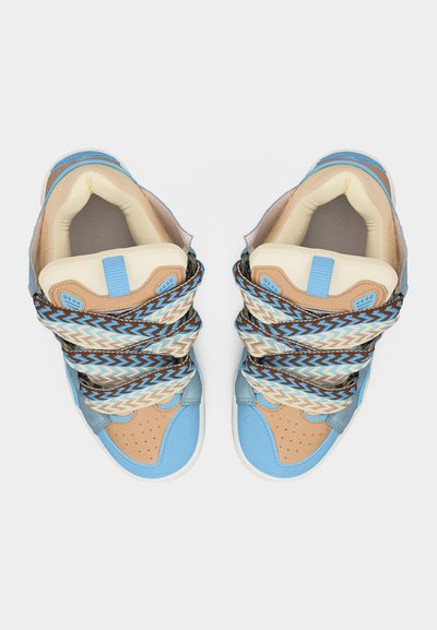 Paire de baskets bleues et beige avec des lacets larges à motifs bleu, blanc et marron, vues de dessus sur un fond blanc.