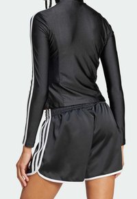 Svart sporttop med hög krage och långa ärmar, kombinerad med svarta shorts med vita ränder och dragsko i midjan.