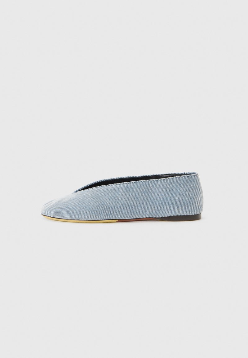 Jeans slip-on sko i lyseblå med en glat overflade, mandelformet tå og en flad sort sål. Minimalistisk design med lav profil.