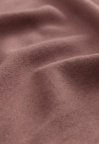 Tessuto in un colore mauve tenue, caratterizzato da una consistenza morbida con una leggera lucentezza e un motivo di tessitura visibile, che mostra pieghe delicate.