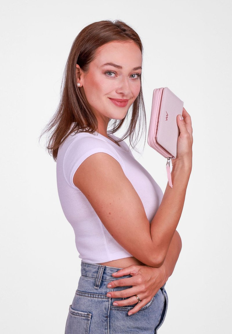 Pink zippered wallet with a textured finish, held against a white background. Features a metallic logo on the front and a wrist strap.