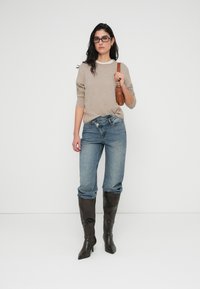 Μπεζ πλεκτό πουλόβερ με χαλαρή εφαρμογή, συνδυασμένο με ανοιχτό μπλε τζιν παντελόνι με γυρισμένα ρεβέρ. Καφέ δερμάτινη τσάντα ώμου, ψηλά σκούρα καφέ μπότες με τακούνι.