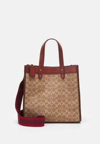 Beige canvas håndtaske med et gentagende cirkulært mønster, brune læderkanter, dobbelte top-håndtag og et aftageligt skulderstrop med røde striber.
