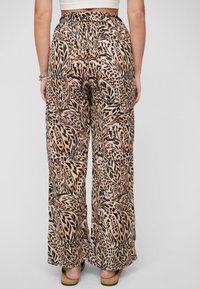 Personne portant un pantalon large taille haute avec un motif animalier brun et noir, associé à des sandales compensées et un crop top blanc.